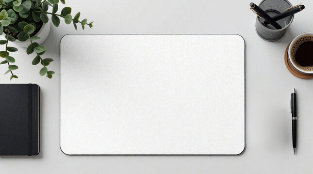 Blank white mousepad on clean desk with plant notebook and coffee cup. Top view of modern workspace with pen holder and writing tools. Minimalist home office setup for productivity and design.