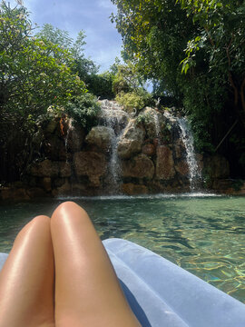 Relaxing on a floating mat in a tropical resort pool with a scenic artificial waterfall and lush green foliage.