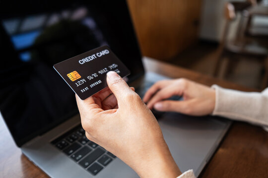Woman holding a credit card while using a laptop for online shopping at cafe. Conceptual image representing e-commerce, digital payment.
