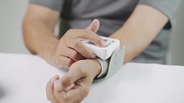 Close up of a senior using a digital wrist blood pressure monitor to check blood pressure at home, representing hypertension management, cardiovascular health, home care, medical monitoring, and welln