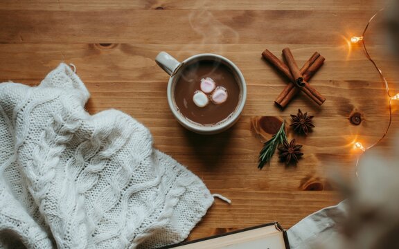 Cozy winter flat lay with hot chocolate mug, knitted sweater, and sparkling lights. Cozy Hot Chocolate with Marshmallows and Cinnamon.