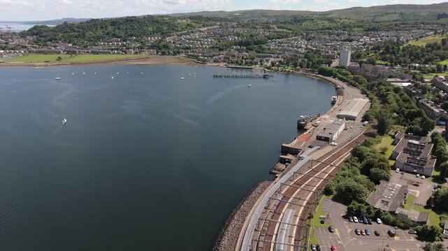 Cinematic aerial drone shot of Gourock railway station and harbor on the Firth of Clyde. Showcases sustainable public transport and coastal urban planning in Scotland.