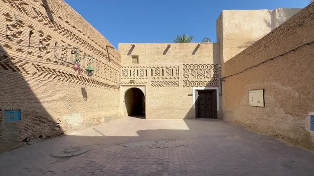 Traditional brick courtyard with carved adobe walls, arched passage and wooden doors in Tozeur medina, Tunisia.