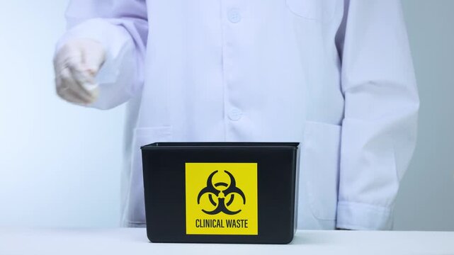 Cautious scientist handles clinical waste management, disposing hazardous material inside biohazard container with professional laboratory safety