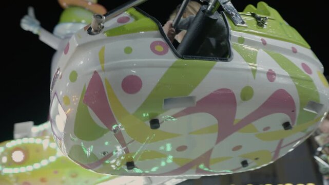 A child smiles while enjoying a colorful amusement park ride featuring vibrant patterns and lights. The attraction moves up and down, creating a fun and thrilling experience