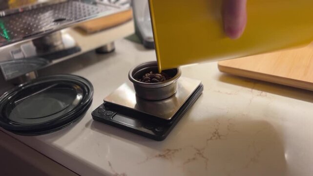 Fresh coffee beans are poured into a grinder on a digital scale before espresso preparation in a modern kitchen, showcasing specialty coffee brewing.