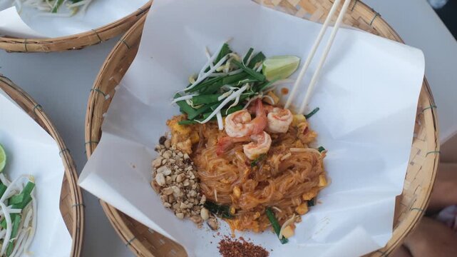 Close-up of a beautifully presented traditional Pad Thai with mixed seafood served in a decorative woven basket plate. Thai food concept