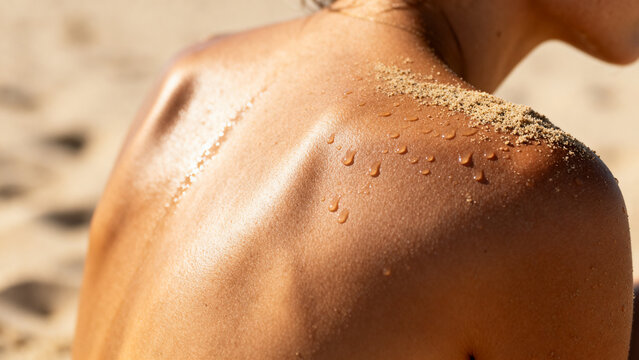 Close up of sun kissed tanned female back with water droplets and sand at sunny beach
