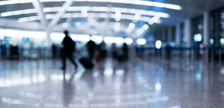 A blurred view of an airport terminal bustling with travelers. The shiny floor reflects lights, creating a lively atmosphere typical of busy travel hubs.