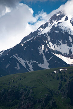 Vertical view of green hills and snowy Mount Kazbek slopes under clouds in Georgia with copy space