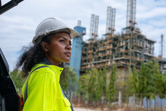 Engineers wearing safety gear, including hard hats examining survey a large blueprint tablet standing industrial facility gas or oil refinery engaged in a job requires high safety standards concept.	