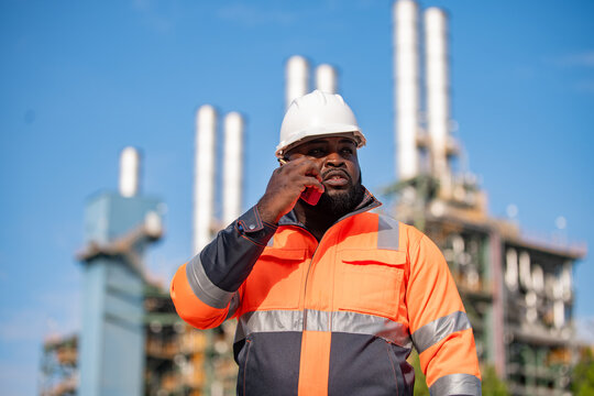 Engineers wearing safety gear, including hard hats examining survey a large blueprint tablet standing industrial facility gas or oil refinery engaged in a job requires high safety standards concept.	