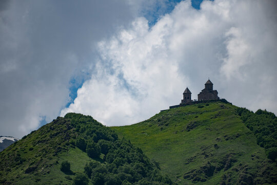 Ancient Gergeti Trinity Church on green hill under cloudy sky in Kazbegi Georgia with copy space