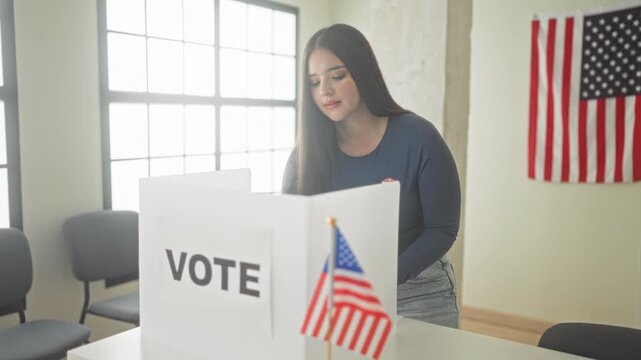 Young woman gives thumbs up at a voting booth inside a building with us flag visible; civic duty pride.