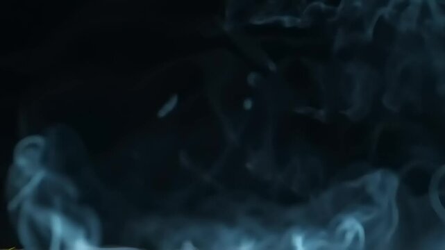 Smoke plumes drift upwards in soft monochromatic grey tones against a completely black backdrop.
