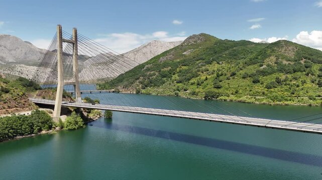 Side aerial view of the bridge deck and cable array over the mountain reservoir