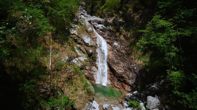 Mountain waterfall plunging directly into a clear emerald rock pool at Pozze Smeraldine in Northern Italy.