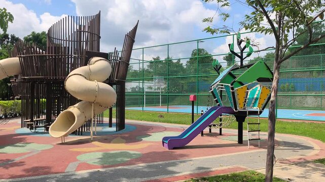 An empty playground features a modern integrated slide structure. The bright recreation area sits under the midday sun. No children are seen playing at this moment, creating a quiet atmosphere.