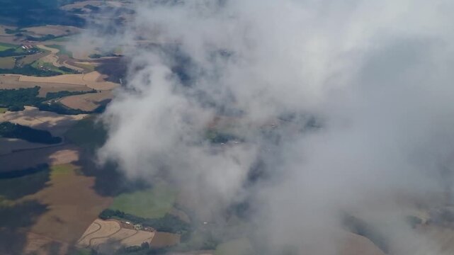 Flying through clouds above Paran&aacute;, Brazil, an aerial window view reveals expansive farmland, rural landscapes, and colorful agricultural patterns stretching across the countryside beneath