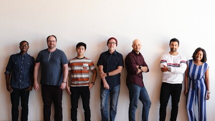 Obraz premium A diverse group of seven people standing against a white wall, smiling.