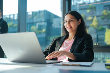 Fototapeta premium Businesswoman using laptop at office desk while checking work online. Professional workspace with computer for remote work, communication, project management and daily business tasks.