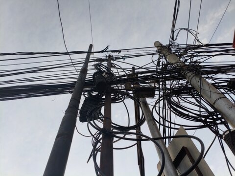 Chaotic tangle of telephone and electrical wires on poles against cloudy sky
