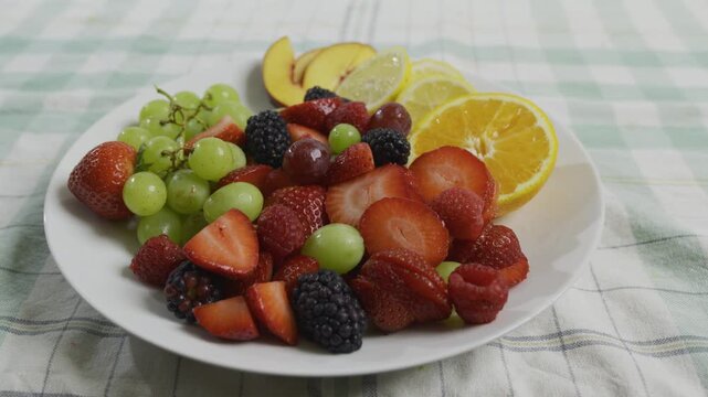 Medium shot of plate filled with strawberries, oranges, lemons, grapes, blackberries, raspberries and peaches