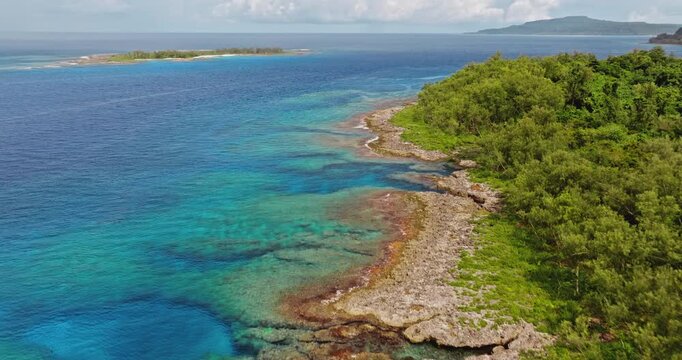 Drone flight over Tegua island coastline in Torres Islands, Vanuatu with lush green tropical trees, rugged rock formations, and clear turquoise ocean revealing coral reef. Aerial view remote landscape