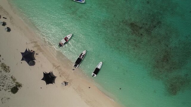 Top down drone view of small boats anchored in crystal clear Caribbean waters beside a white sand beach in Los Roques, Venezuela.