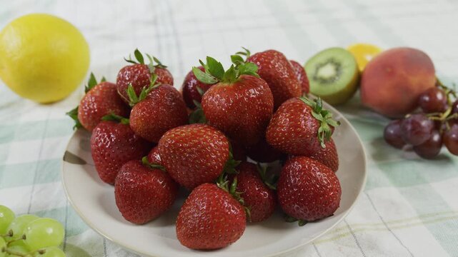 Stacked strawberries on small plate near other fruit - tracking, medium shot