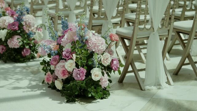 Wedding aisle decorated with rose flower arrangements beside white chairs