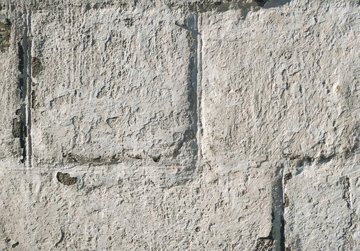 Light gray, almost white cinder block wall covered with lime chalk water-based paint. Old stone surface texture. Close-up.