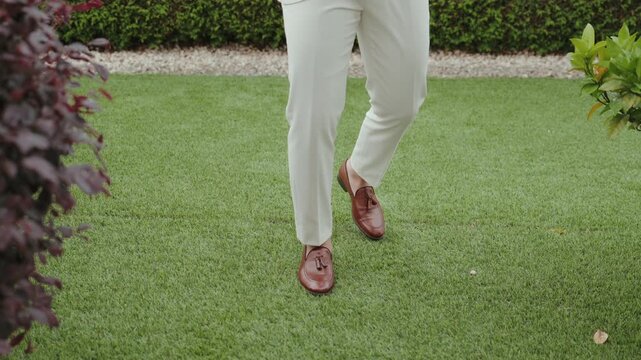 Man in white trousers and brown loafers walking across green lawn
