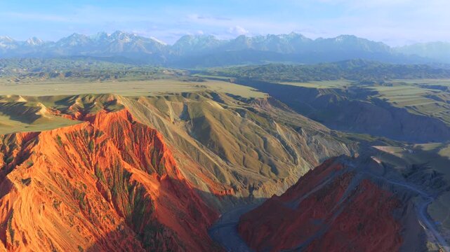 Aerial view of Anjihai Grand Canyon in Xinjiang, colorful stratified rock landforms and braided river with Tianshan snow mountains background