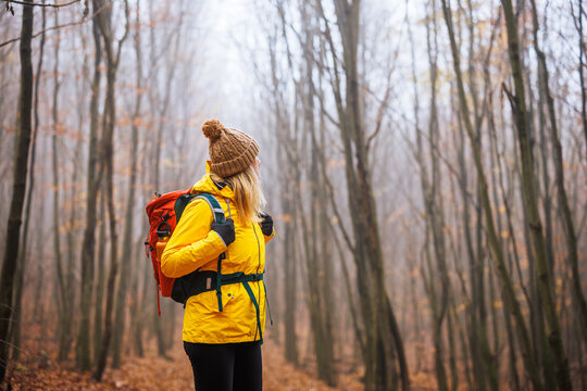 Tourist with backpack hiking in fog at forest. Woman wearing sport clothing for autumn active lifestyle. Adventure at nature