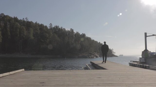 Man walking alone on a wooden pier, looking at the calm water of the Oslo fjord in Bygdoy, Norway