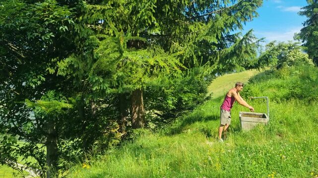 A man cools down with fresh mountain water from a cattle fountain in the Swiss Alps, framed by green alpine pastures and stunning summer landscapes during a warm day