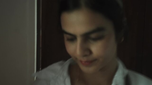 Woman in white shirt walks through dimly lit home interior into brighter room