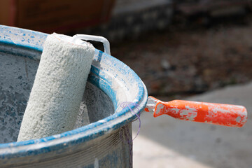 Close-up of a paint roller resting inside a paint bucket at a residential construction site. The image represents house painting, renovation work and professional finishing before project completion. © VikSid