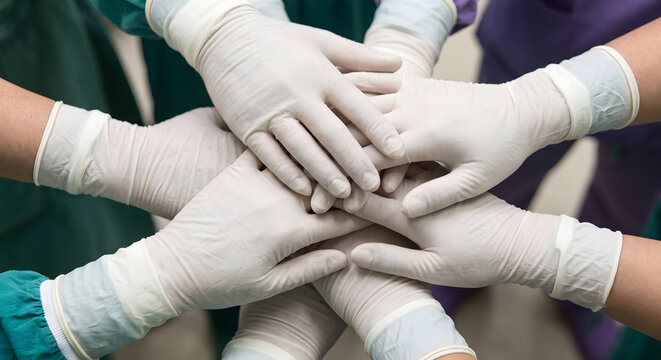 Healthcare professionals hands in medical gloves stacked together showing unity and teamwork in hospital setting.