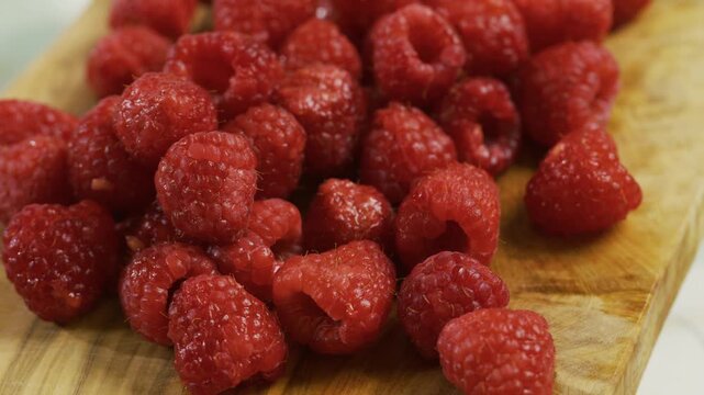 Cluster of bright, fresh raspberries on cutting board - closeup