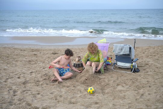 Mother and son building a sand sculpture together on the beach during a peaceful cloudy summer day, enjoying creative family time and making lasting vacation memories by the sea