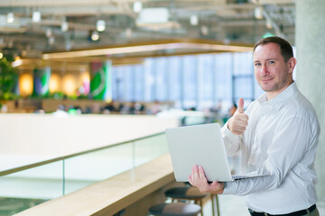 Fototapeta premium Caucasian businessman holding laptop showing thumbs up in office