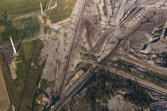 Aerial view of the Schleenhain lignite open cast mine featuring deep excavation pits, industrial conveyor paths, and wind turbines in Zwenkau, Saxony, Germany.