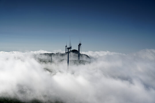 Aerial view of wind turbines on Bica da Cana peak rising above a dense sea of clouds under a clear blue sky in Funchal, Madeira, Portugal.