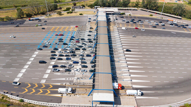Aerial view of Milano Sud toll plaza on the A1 motorway with vehicles and trucks passing through toll gates and highway infrastructure in Melegnano, Lombardy, Italy.