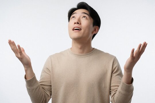 Young Asian man looks up with amazed expression and open hands. He seems surprised or hopeful, perhaps asking for something or receiving good news. His gesture conveys wonder and positive outlook.