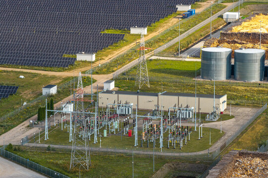 Aerial view of an electrical substation and adjacent solar farm with power lines, transformers, and storage tanks in a rural landscape in Poland.