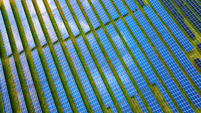 Aerial view of a modern solar park with rows of photovoltaic panels arranged in neat lines across a green field in Germany.