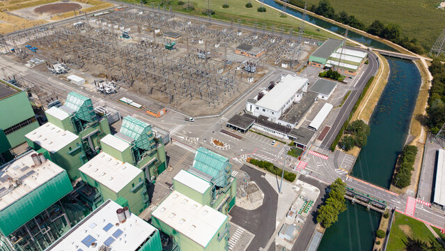 Aerial view of the TTEP Tavazzano thermal power plant and TERNA electrical substation with industrial buildings, power lines, and a nearby canal in Tavazzano con Villavesco, Lombardy, Italy.
